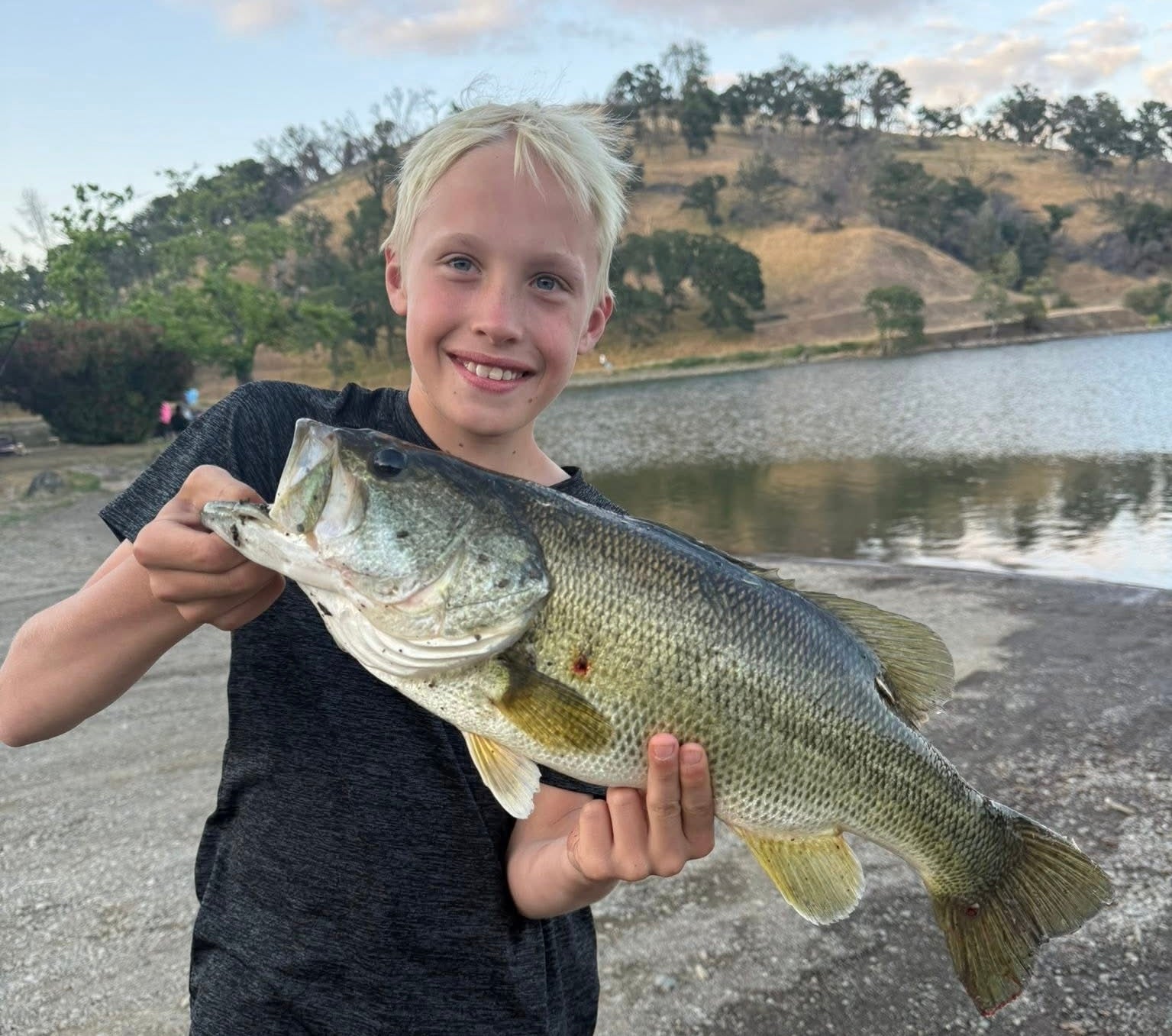 Young boy holding a large fish by a lake with hills in the background