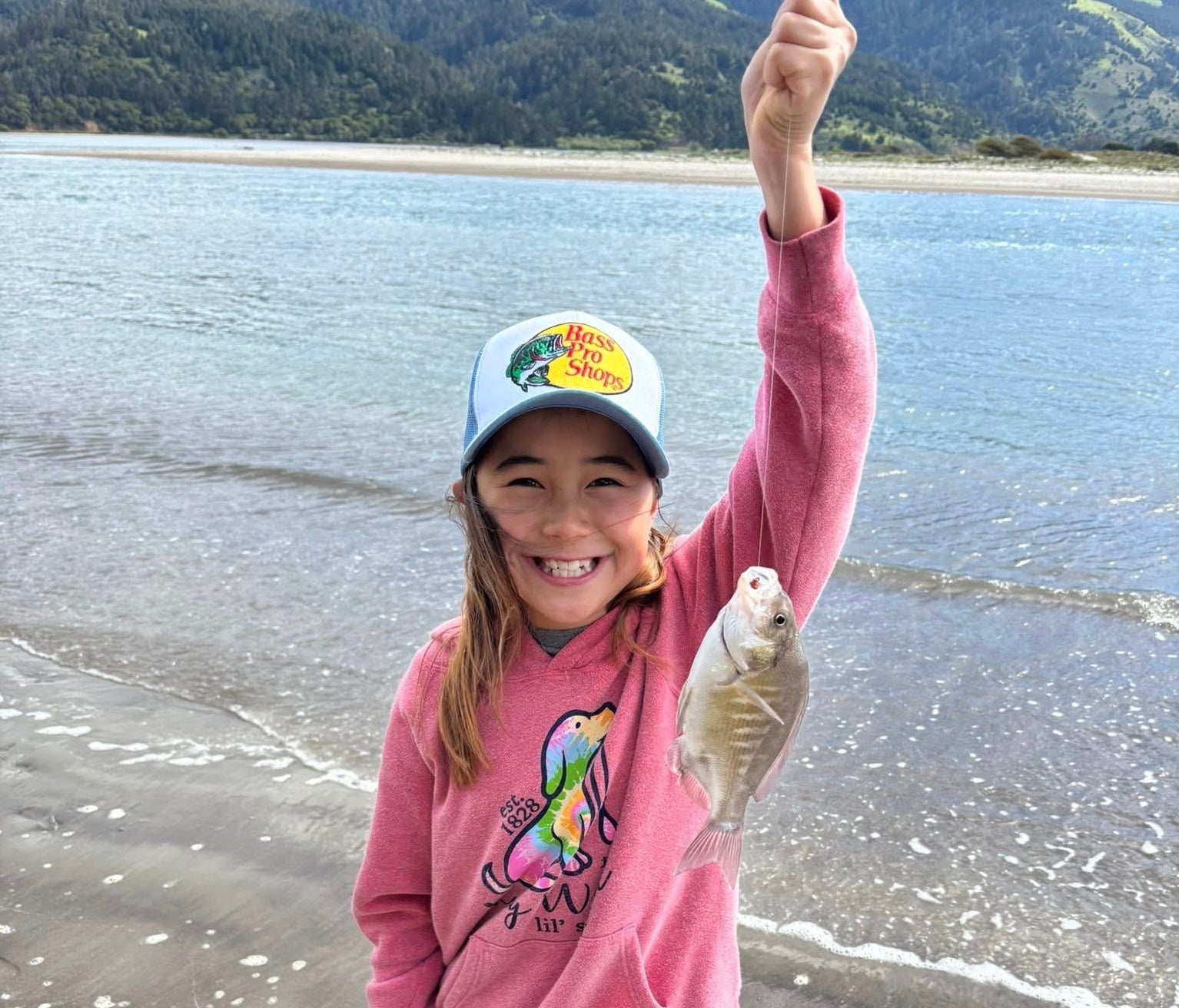 Child holding a fish on a beach with mountains in the background
