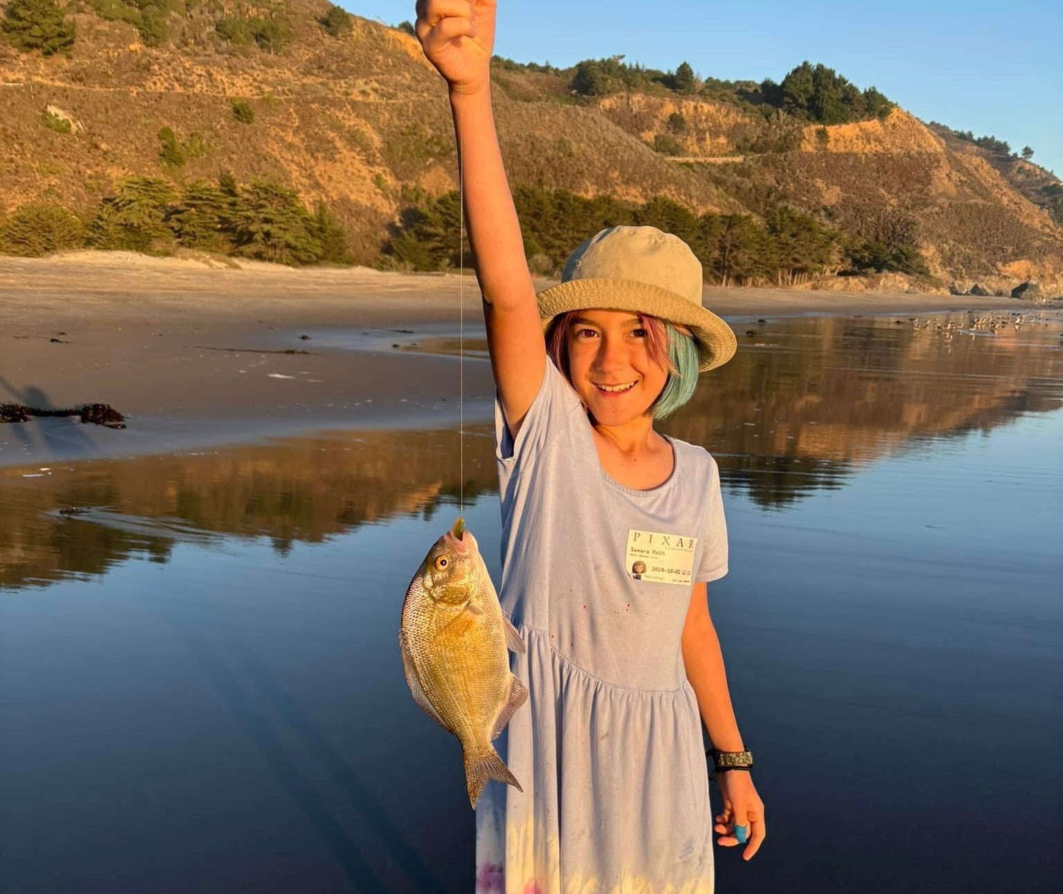 Child holding a fish on a beach with mountains in the background